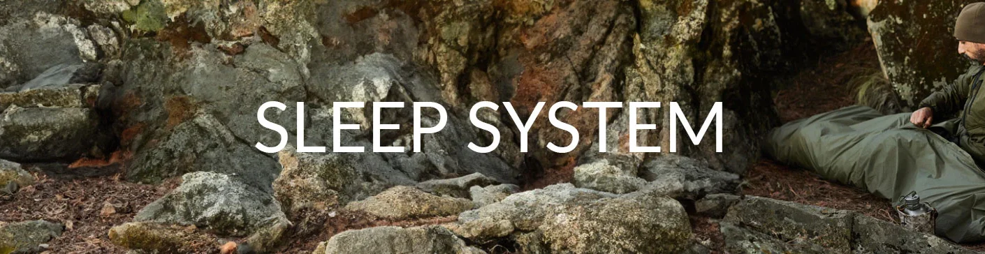 Person using Snugpak Special Forces Sleeping System in a rocky outdoor setting, emphasizing modular sleeping solution for extreme weather conditions.
